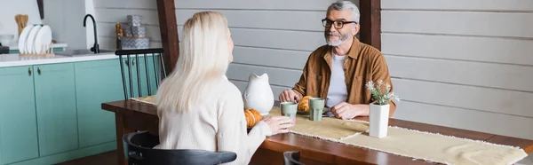 Homme âgé en lunettes regardant femme près du petit déjeuner dans la cuisine, bannière — Photo de stock