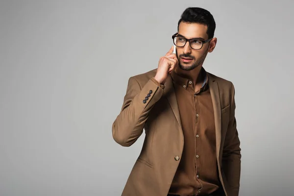 Hombre de negocios árabe en ropa formal marrón hablando en un teléfono inteligente aislado en gris - foto de stock