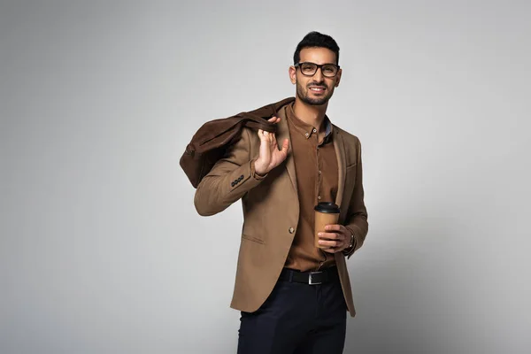 Homme d'affaires arabe souriant tenant du café pour aller et sac à main isolé sur gris — Photo de stock