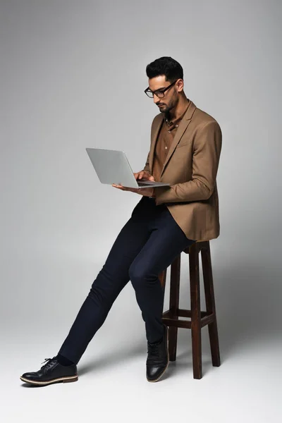 Homem de negócios árabe usando laptop na cadeira no fundo cinza — Fotografia de Stock