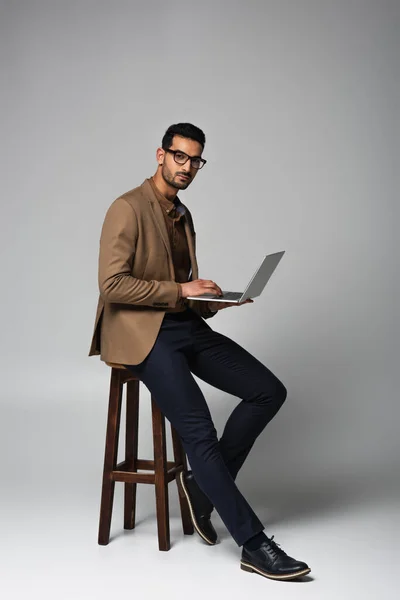 Arabian businessman using laptop and looking at camera on chair on grey background — Stock Photo