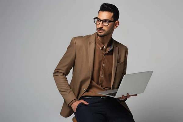 Muslim manager in suit holding laptop isolated on grey — Stock Photo