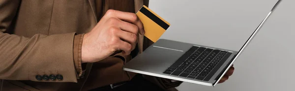 Ausgeschnittene Ansicht eines Mannes in offizieller Kleidung mit Kreditkarte und Laptop isoliert auf grau, Banner — Stockfoto