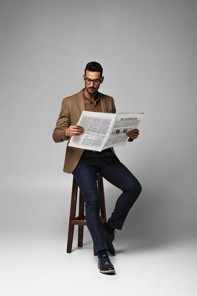 Homem de negócios árabe lendo notícias de negócios na cadeira em fundo cinza — Fotografia de Stock