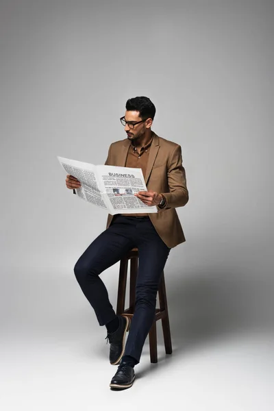 Muslim businessman reading business newspaper on chair on grey background — Stock Photo