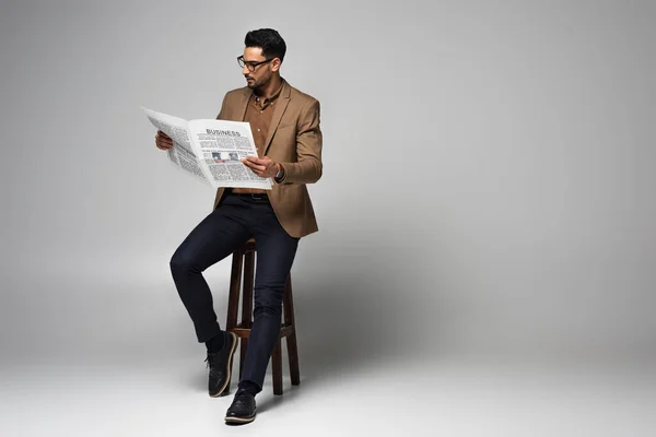 Gut aussehender muslimischer Geschäftsmann liest Nachrichten auf Stuhl auf grauem Hintergrund — Stockfoto