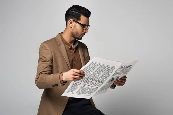 Vue latérale d'un homme d'affaires arabe portant des lunettes lisant des nouvelles isolées sur le gris — Photo de stock