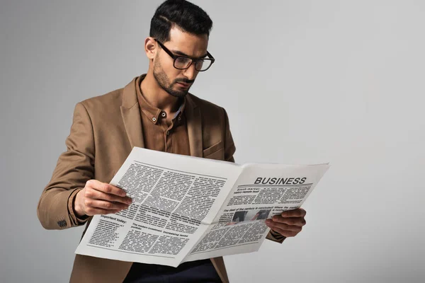 Arabian businessman in suit and eyeglasses reading business news isolated on grey — Stock Photo