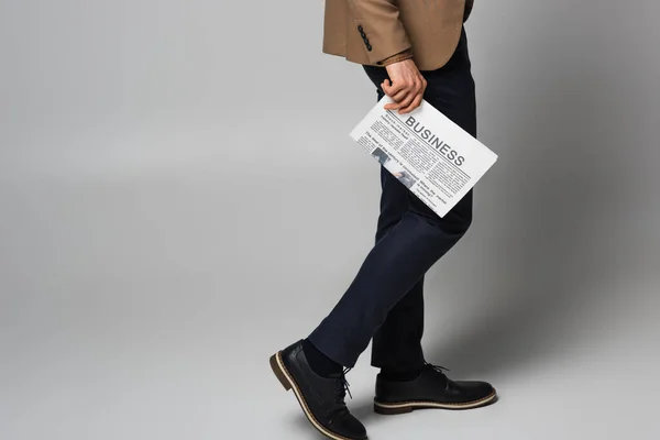 Cropped view of newspaper with business lettering in hand of man in suit on grey background — Stock Photo