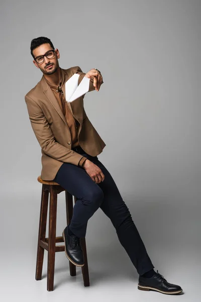 Muslim businessman throwing paper plane while sitting on chair on grey background — Stock Photo