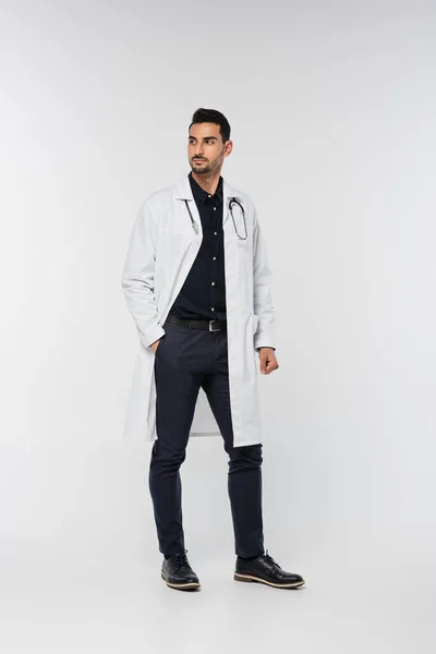 Arabo medico in cappotto bianco guardando altrove su sfondo grigio — Foto stock