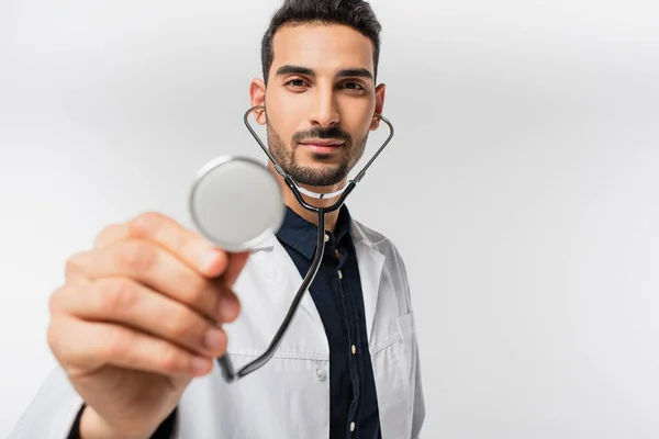 Medico arabo in possesso di stetoscopio offuscata e guardando la fotocamera isolata su grigio — Foto stock