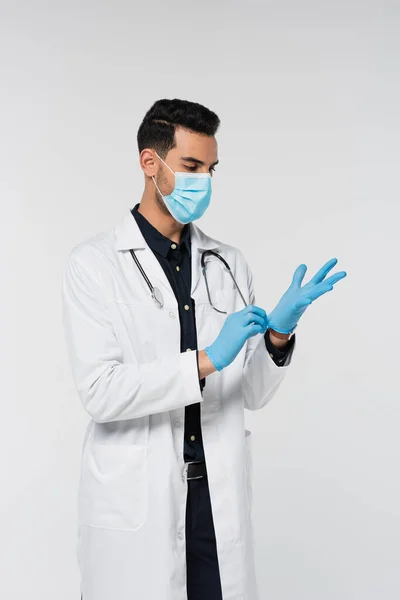 Médico muçulmano em máscara médica e casaco branco usando luvas de látex isolado em cinza — Fotografia de Stock