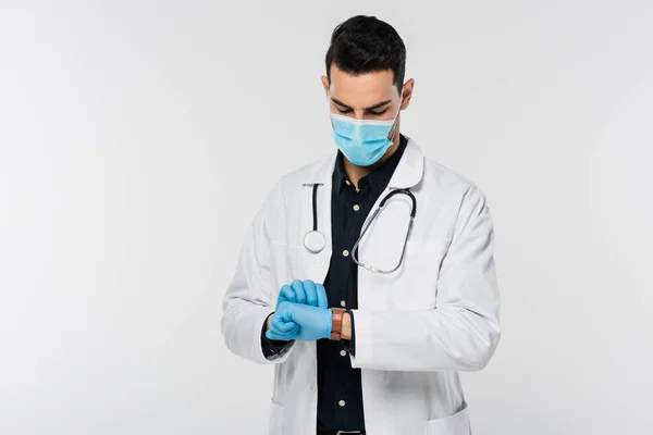 Мусульманський лікар в медичній масці і латексні рукавички дивлячись на наручний годинник ізольований на сірому — стокове фото