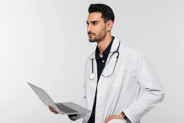 Young muslim doctor holding laptop and looking away isolated on grey — Stock Photo