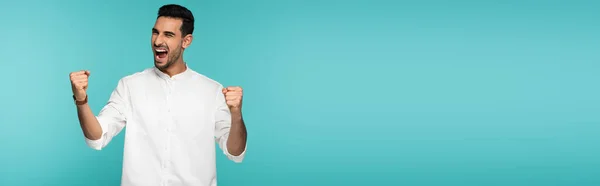 Hombre musulmán excitado en camisa blanca mostrando sí gesto aislado en azul, bandera - foto de stock