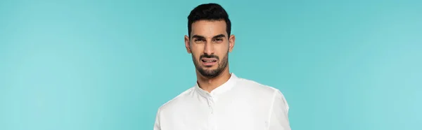 Confused arabian man in white shirt looking at camera isolated on blue, banner — Stock Photo