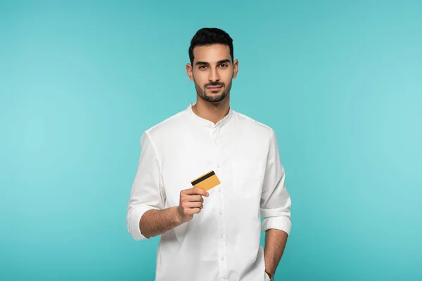 Giovane uomo musulmano in possesso di carta di credito isolato su blu — Foto stock