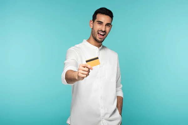 Hombre árabe alegre mostrando tarjeta de crédito aislado en azul - foto de stock