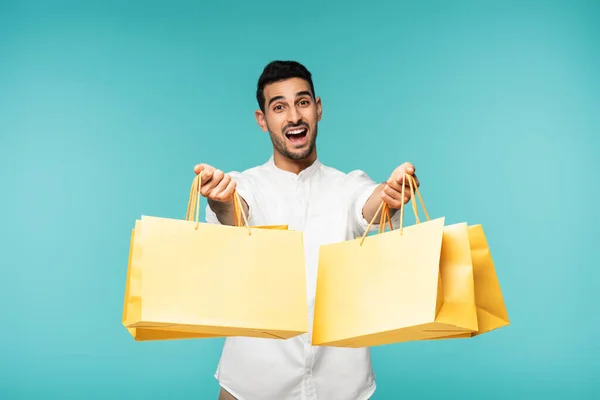 Homme arabique excité tenant des sacs à provisions isolés sur bleu — Photo de stock