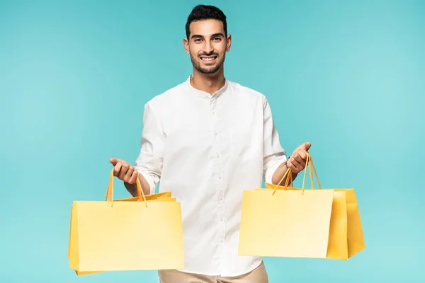Positivo uomo arabo che tiene borse della spesa gialle isolate su blu — Foto stock