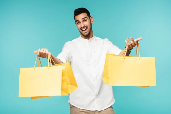 Hombre musulmán feliz sosteniendo gas de compras con compras aisladas en azul - foto de stock
