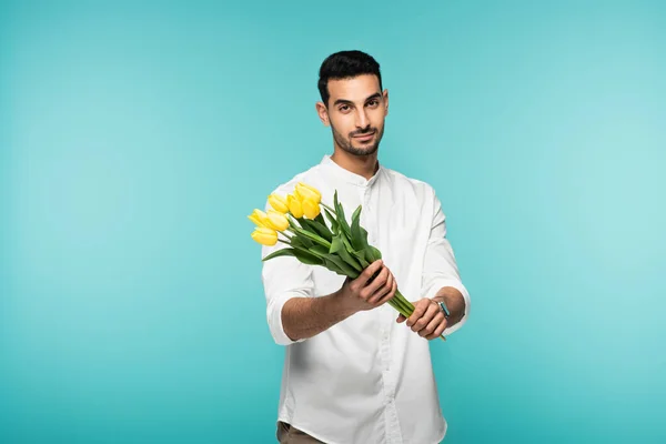 Hombre musulmán con camisa blanca sosteniendo flores aisladas en azul - foto de stock
