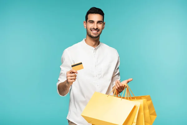 Joven musulmán con tarjeta de crédito y bolsas aisladas en azul - foto de stock