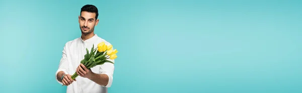 Young arabian man holding tulips isolated on blue, banner — Stock Photo