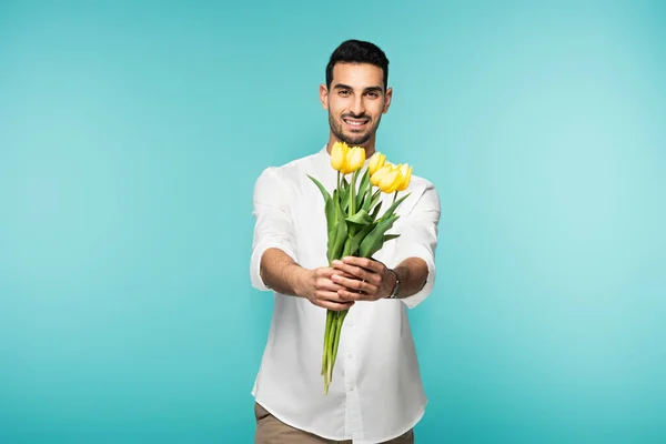 Uomo arabo sorridente che tiene fiori gialli isolati su blu — Foto stock