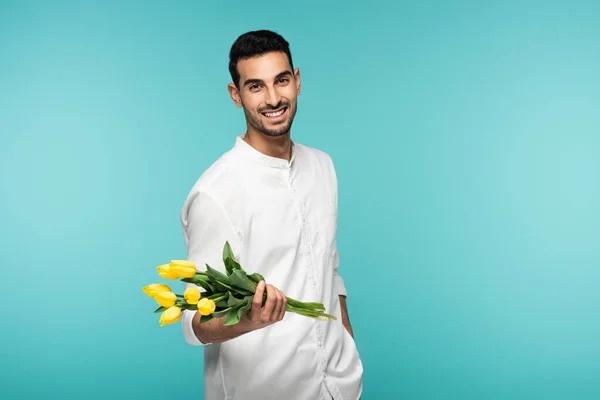 Cheerful arabian man holding tulips isolated on blue — Stock Photo