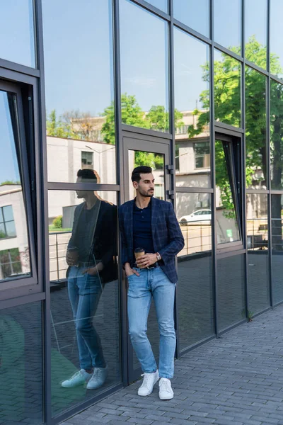 Hombre de negocios árabe sosteniendo café para ir cerca de la construcción al aire libre - foto de stock