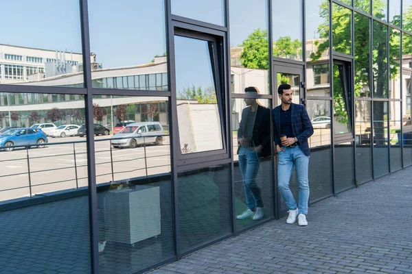 Young muslim businessman holding hand in pocket and paper cup near building — Stock Photo