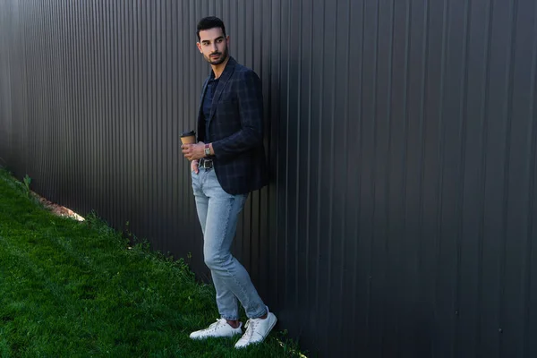 Young muslim businessman holding coffee to go near fence outdoors — Stock Photo