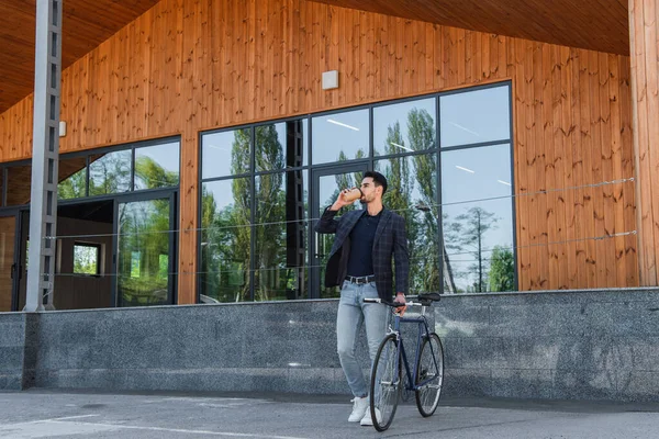 Muslim businessman drinking coffee near bicycle outdoors — Stock Photo