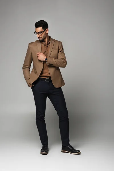 Hombre de negocios árabe en gafas de vista mirando chaqueta sobre fondo gris - foto de stock