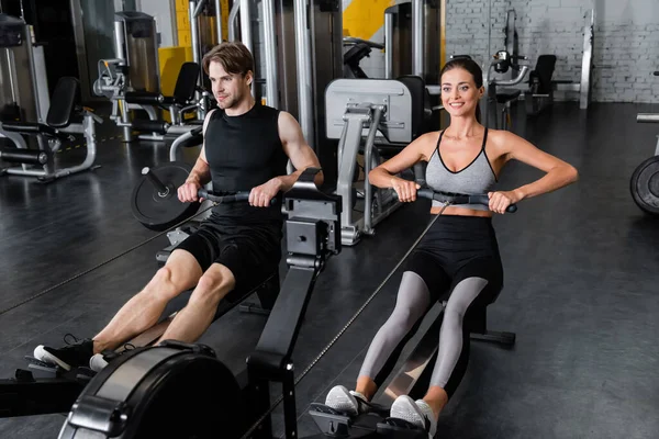 Smiling sportsman and sportswoman working out on pull rope training machines — Stock Photo