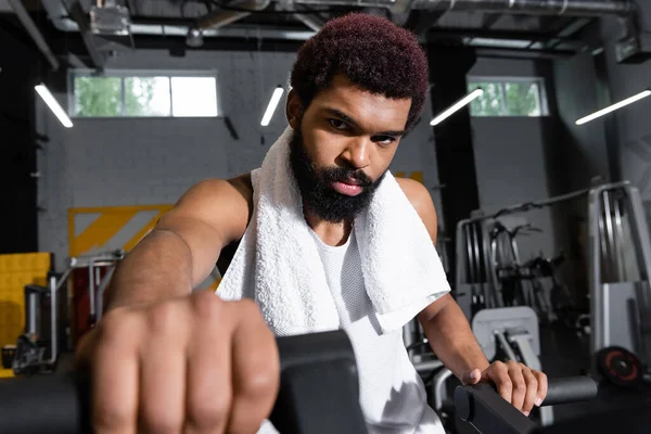 Fiducioso sportivo afroamericano guardando la fotocamera mentre si allena in palestra in primo piano sfocato — Foto stock