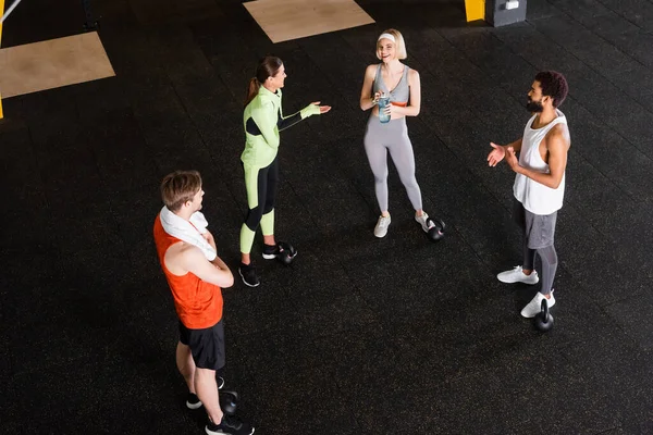 Vue grand angle des personnes souriantes interracial en vêtements de sport parler dans la salle de gym — Photo de stock