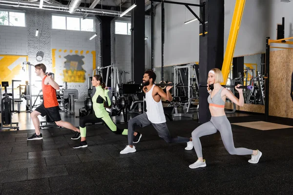 Young multiethnic sports people doing forward lunges with gymnastic sticks — Stock Photo