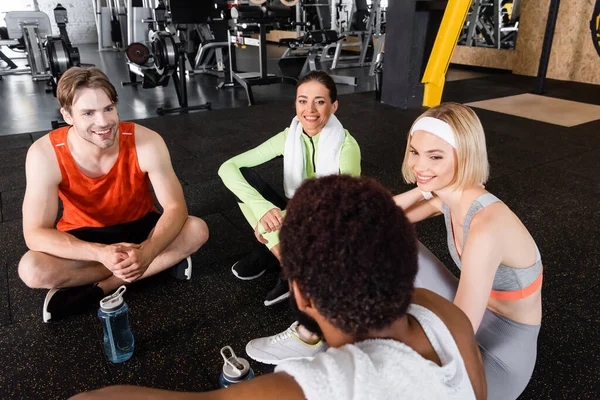 Happy multiethnic people sitting on floor and talking in sports center — Stock Photo