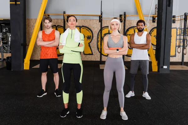 Vista completa de personas multiétnicas en ropa deportiva de pie con los brazos cruzados en el gimnasio - foto de stock