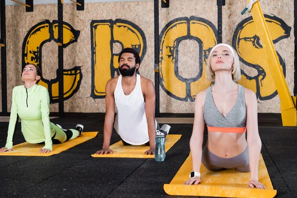 Young interracial people meditating in cobra pose in gym — Stock Photo