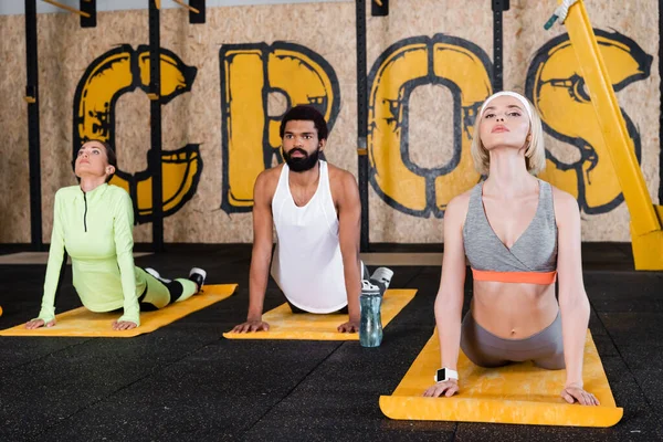 Jeunes sportifs multiethniques s'entraînant au cobra posent sur des tapis de fitness — Photo de stock