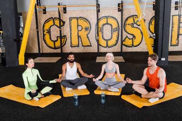 Personas multiétnicas meditando en la pose de loto con los ojos cerrados en las alfombras de fitness - foto de stock