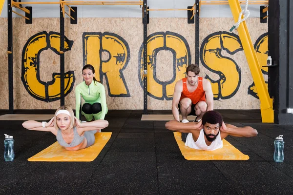 Jeunes entraîneurs aidant les sportifs interraciaux faisant de l'exercice abs dans la salle de gym — Photo de stock