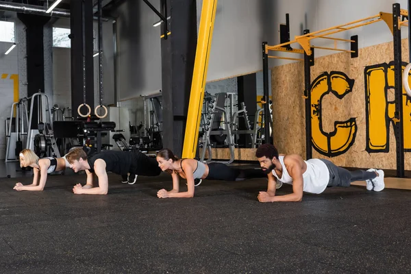 Jóvenes deportistas multiétnicos entrenando en tablón posan en gimnasio - foto de stock