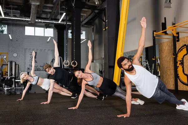 Група міжрасових людей тренується в боковій дошці позу в спортзалі — стокове фото