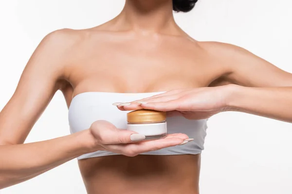 Vue partielle de la jeune femme en soutien-gorge blanc tenant récipient à crème dans les mains isolées sur blanc — Photo de stock