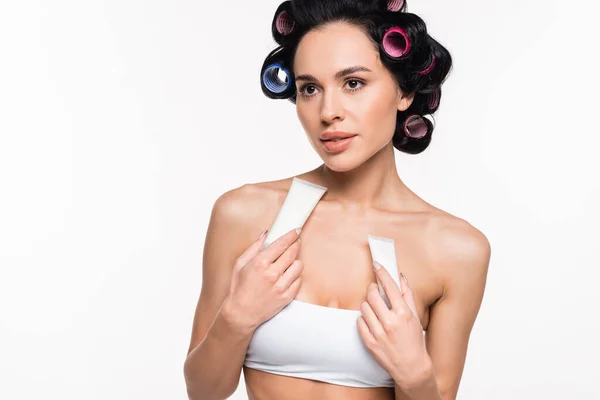 Young woman in top and curlers holding cream tubes near breast isolated on white — Stock Photo